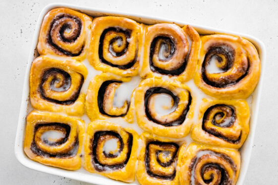 Vegan pumpkin cinnamon rolls in a baking dish with icing.