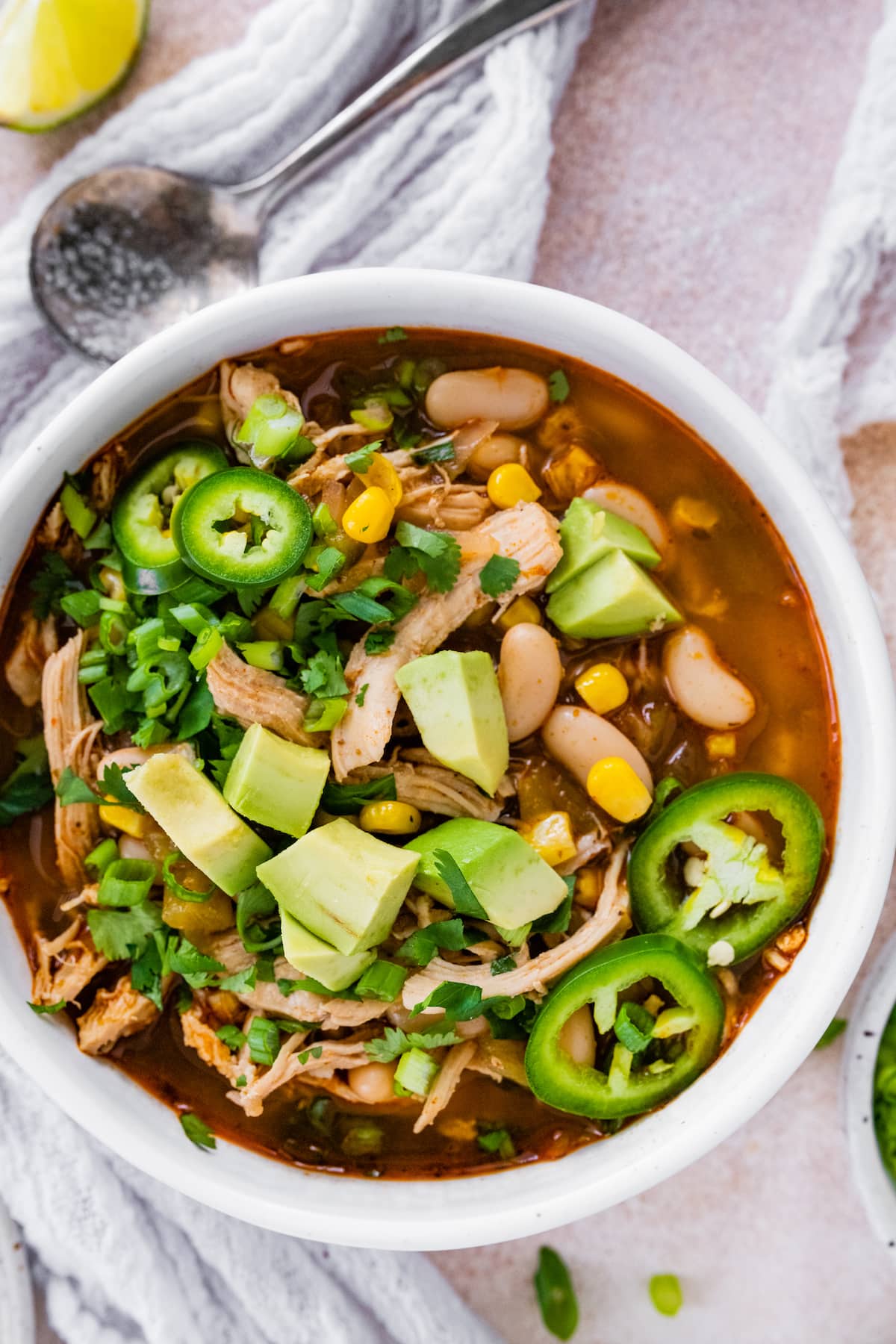 A bowl of white bean chicken chili topped with jalapeños and avocado.