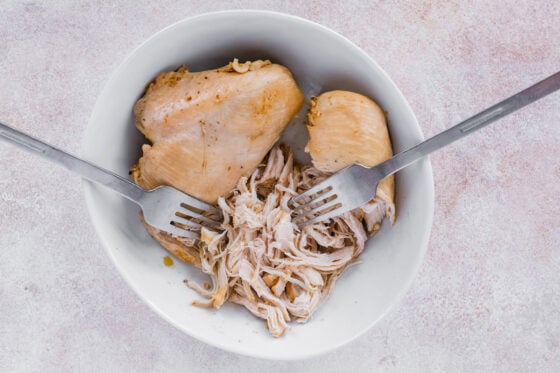 Shredding chicken in a bowl with two forks.