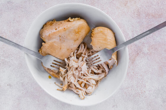 Shredding chicken in a bowl with two forks.