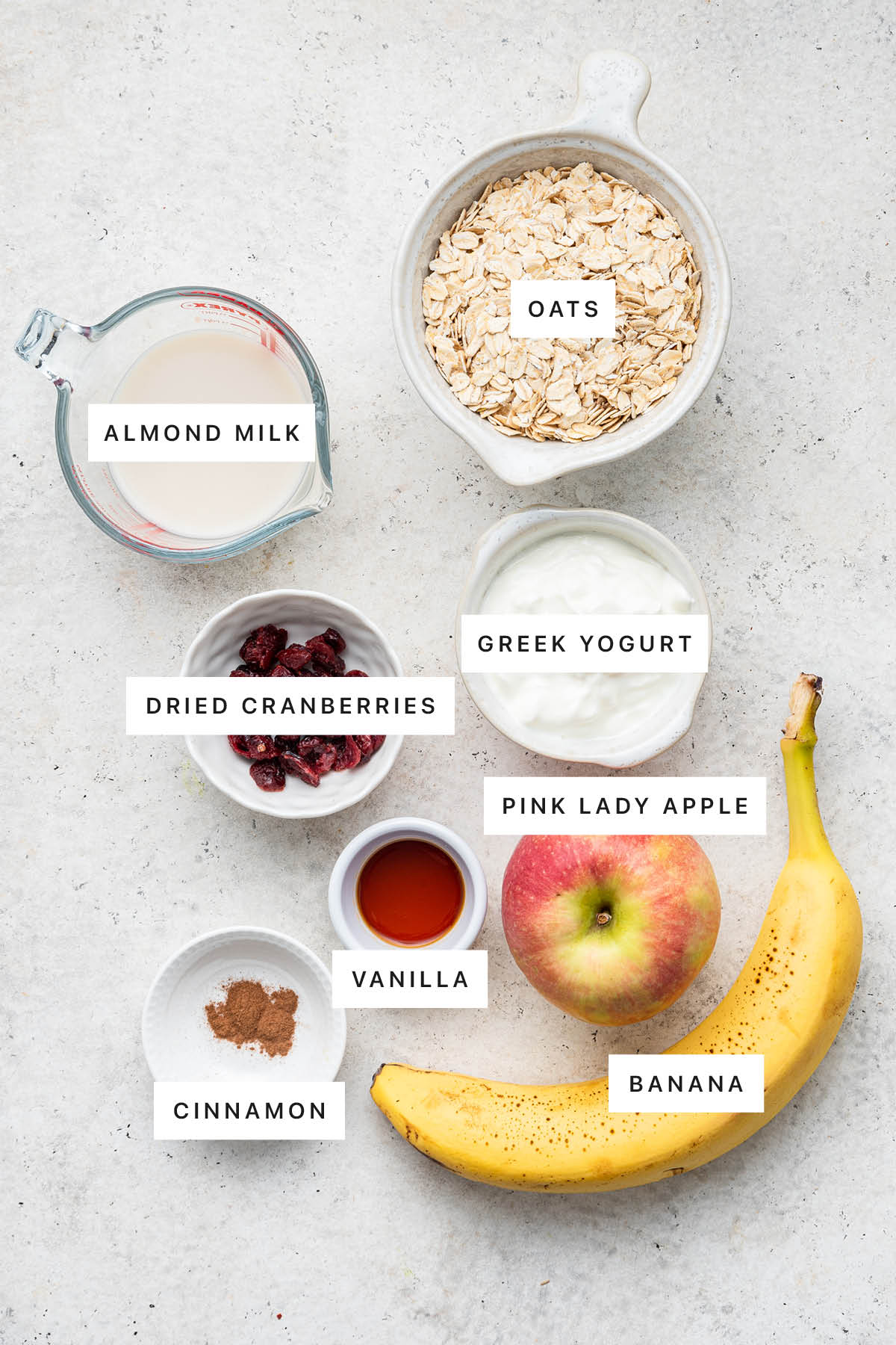 Ingredients measured out to make Chilled Swiss Oatmeal: almond milk, oats, Greek yogurt, dried cranberries, pink lady apple, vanilla, cinnamon and banana.