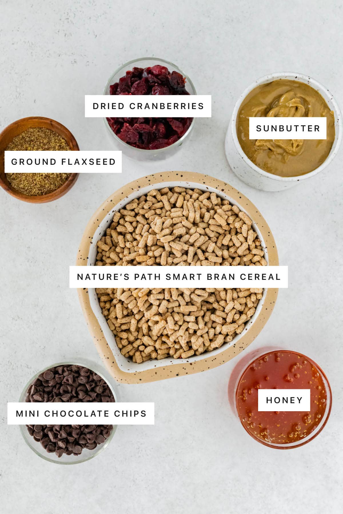 Ingredients measured out to make No Bake High Fiber Bars: ground flaxseed, dried cranberries, sunbutter, bran cereal, mini chocolate chips and honey.