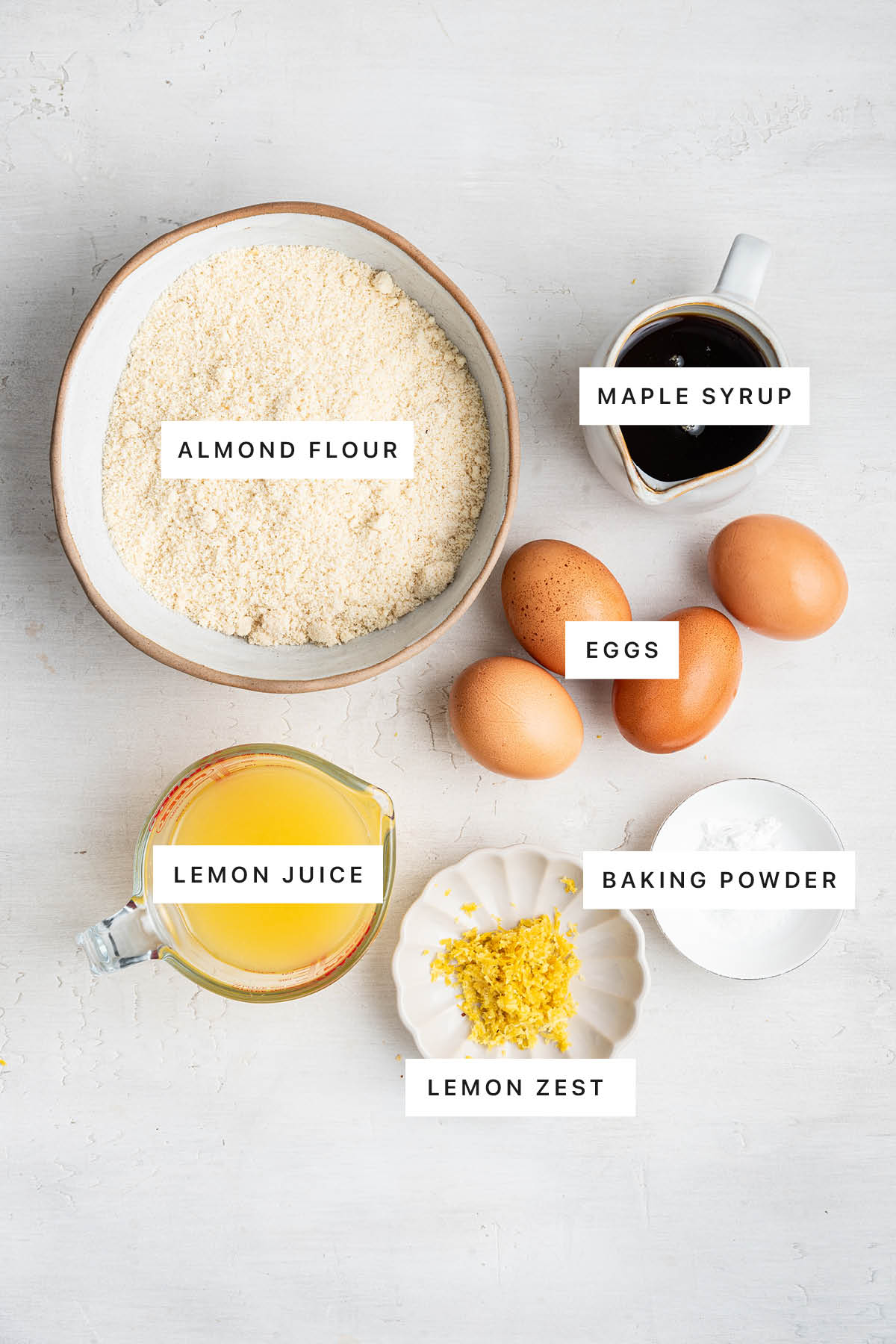 Ingredients measured out to make Healthy Lemon Bars: almond flour, maple syrup, eggs, lemon juice, lemon zest and baking powder.