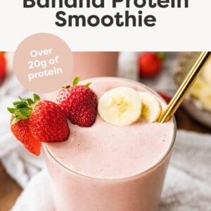 Glass of a strawberry banana protein smoothie served with fresh strawberries, banana and a gold straw.