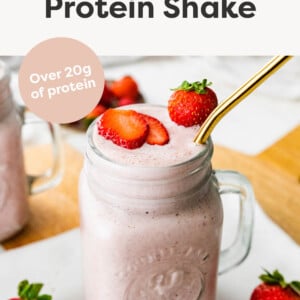 Strawberry Protein Shake in a mason jar glass with a gold straw and topped with strawberries.