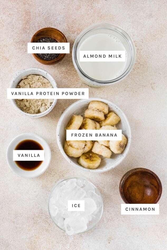 Almond milk, frozen banana, vanilla protein powder, vanilla bean, chia seeds and cinnamon measured out to make a vanilla protein shake.