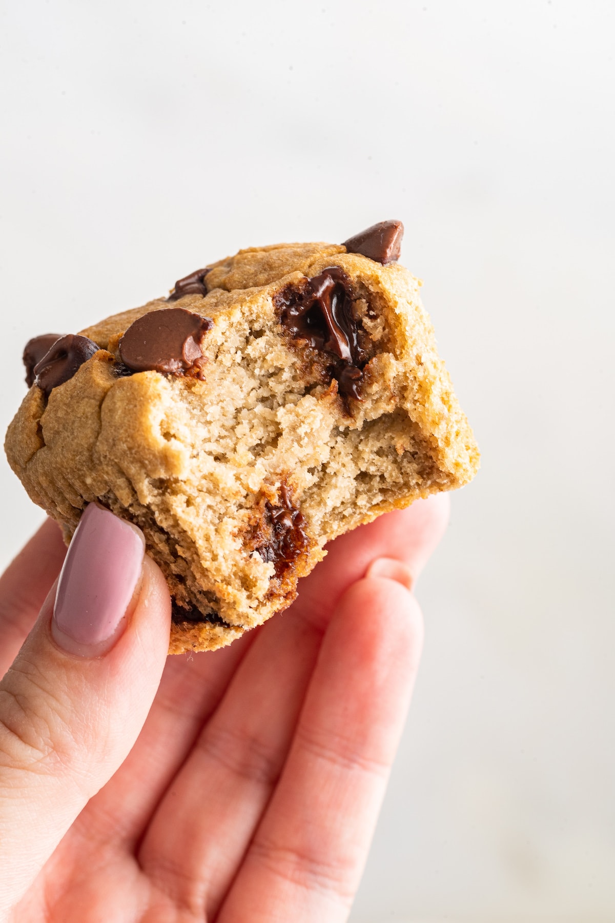 A hand holding up a banana muffin with a bite taken out of it.