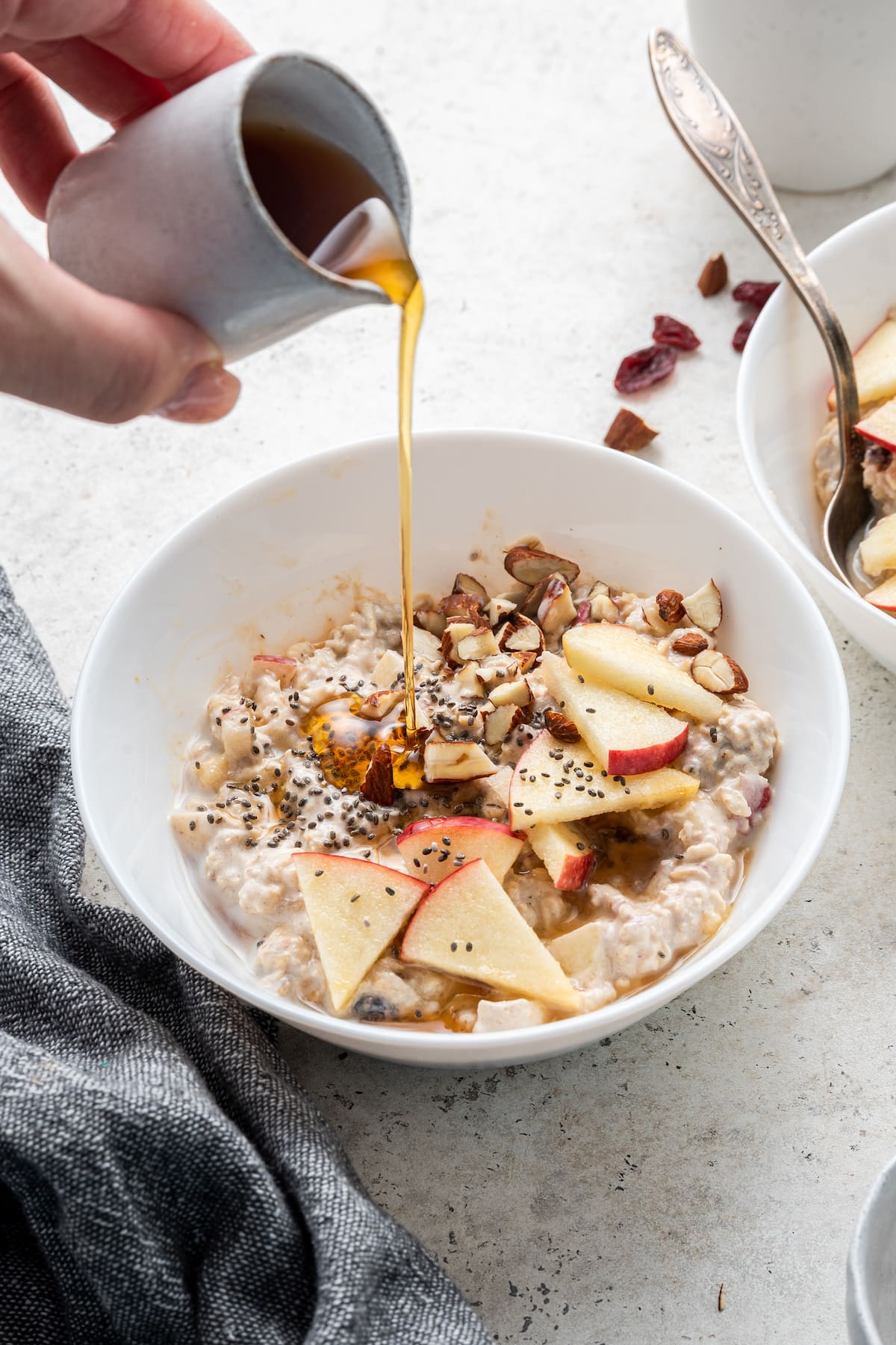 Woman's hand pouring maple syrup over bowl of bircher muesli.