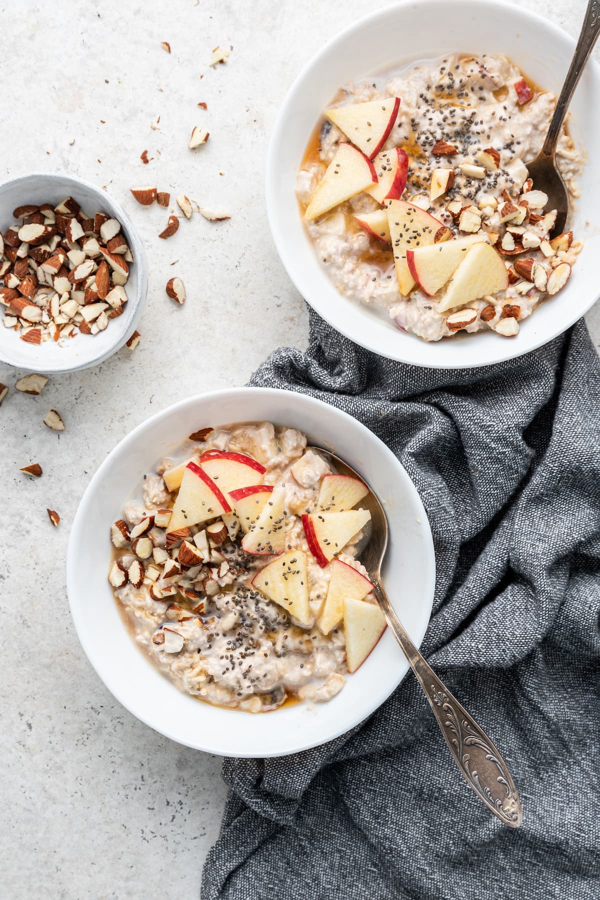 Two white bowls of bircher muesli with spoons in them.