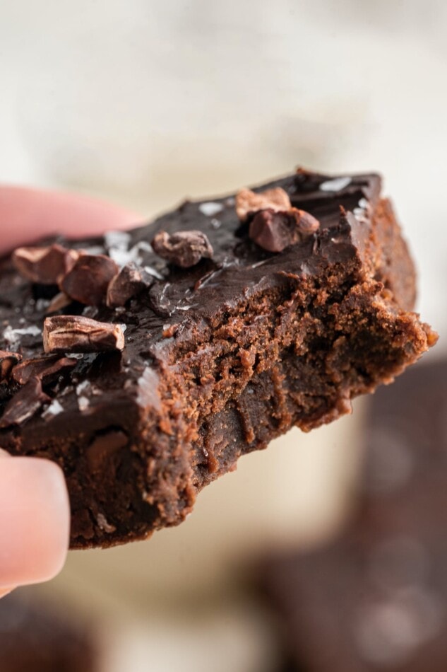 A hand holding up a chickpea brownie that has had a bite taken out of it.