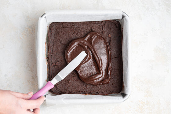 Spreading chocolate ganache across the top of the baked chickpea brownies.