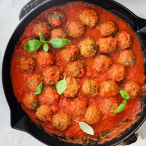 Spinach turkey meatballs with pasta sauce in a cast iron skillet.