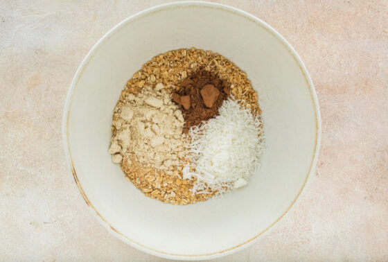 Cereal and oat mixture in a large mixing bowl with coconut, protein and cocoa powder.