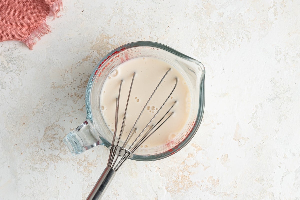 Almond milk and apple cider vinegar mixed together in a glass measuring cup with a whisk.