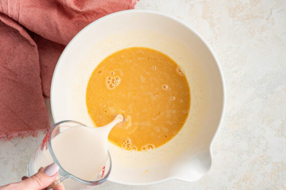 Adding the almond milk and apple cider vinegar mixture to eggs then add maple syrup, Greek yogurt and vanilla extract mixed together in a bowl.