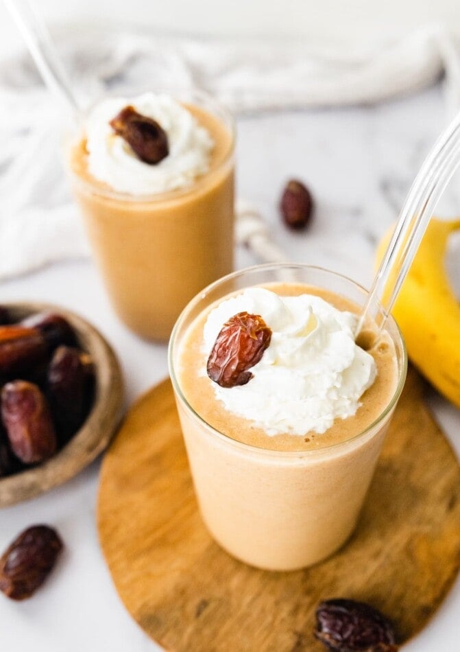 Two healthy date shakes topped with whipped cream and a date.