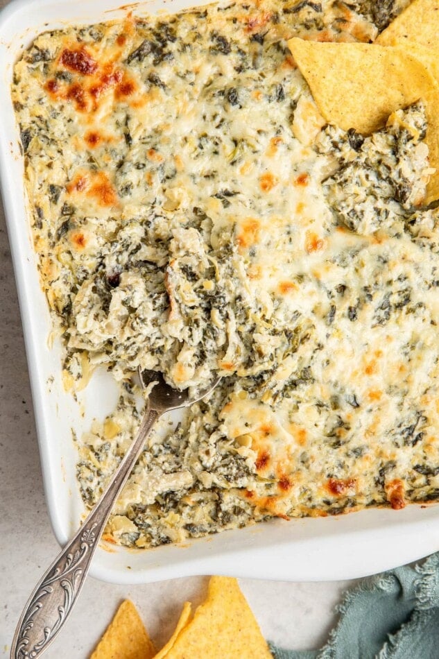 A serving spoon resting in spinach artichoke dip.