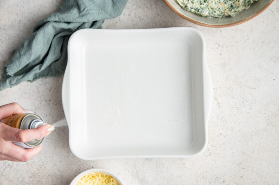 Spraying an 8x8 baking dish with oil.