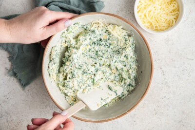 Cheese mixed into the spinach artichoke mixture in a bowl.