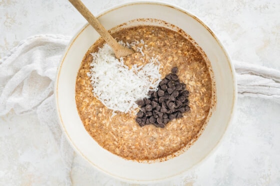 Folding in shredded coconut and chocolate chips into an oatmeal mixture.