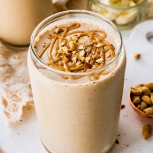 Close up of a peanut butter protein shake in a glass with a drizzle of peanut butter and chopped peanuts on top.