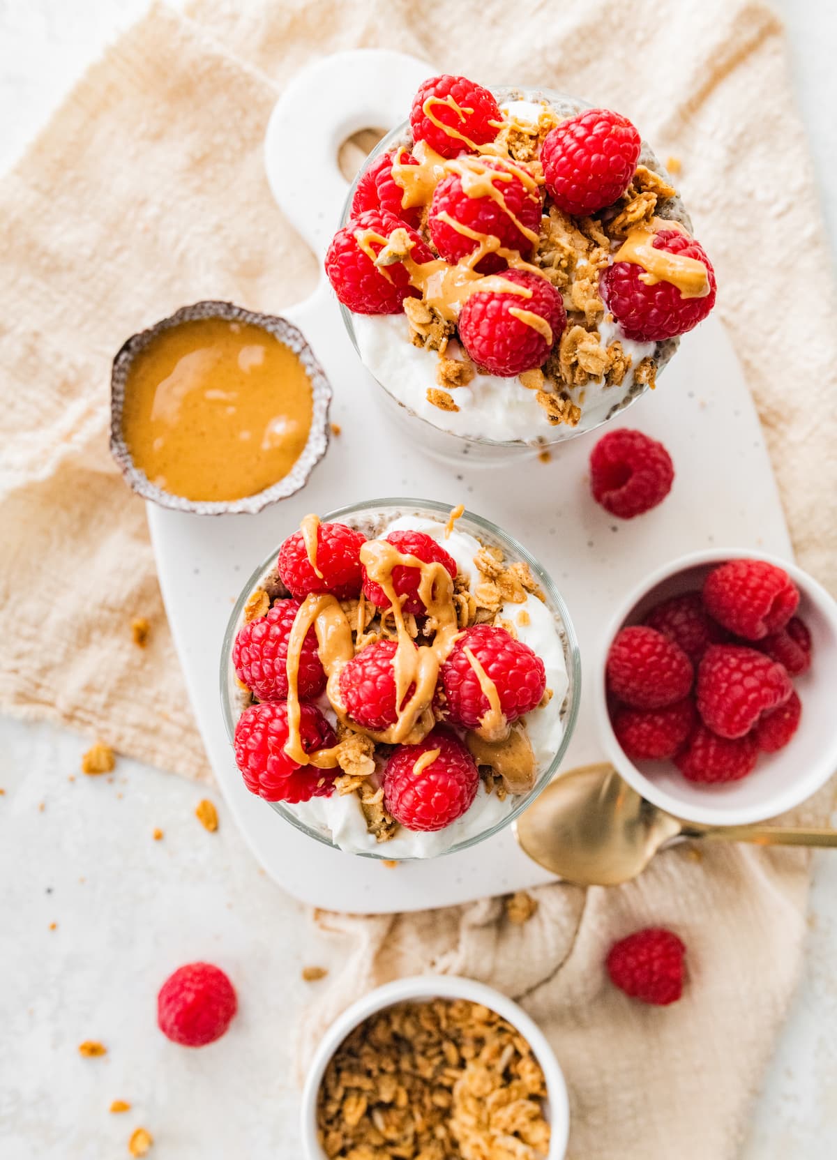 Two jars of protein chia pudding topped with fresh raspberries, greek yogurt and a drizzle of nut butter.