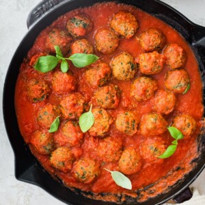 Spinach turkey meatballs with pasta sauce in a cast iron skillet.