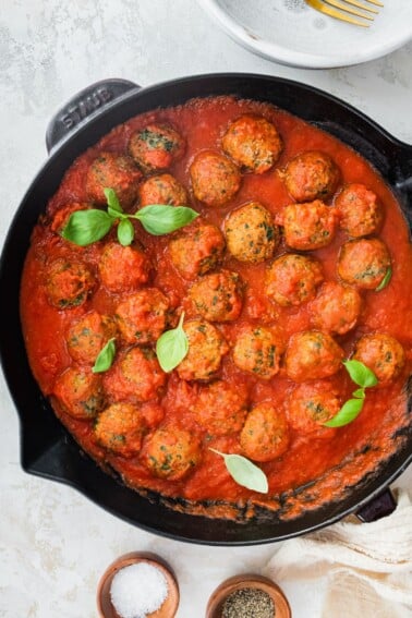 Spinach turkey meatballs with pasta sauce in a cast iron skillet.