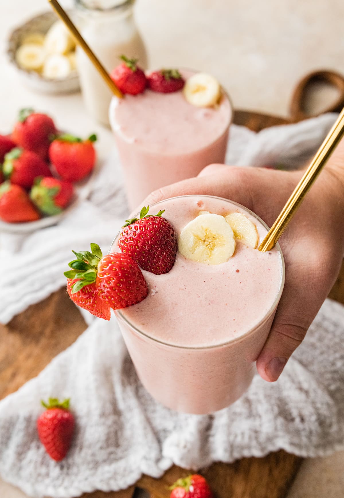 A hand holding up a glass of strawberry banana protein smoothie.