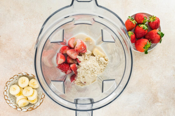 Ingredients for a strawberry banana protein smoothie in a high-powered blender.