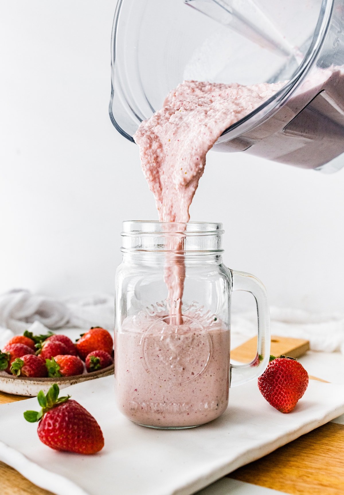 Pouring a strawberry protein shake from a blender to a jar.
