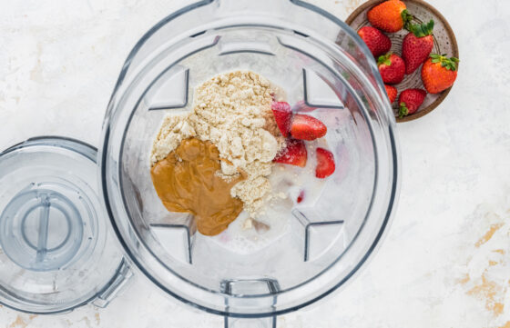 Ingredients for strawberry protein shake in a high-powered blender.