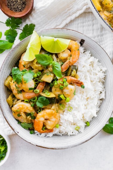 A bowl of thai green curry with shrimp and rice.