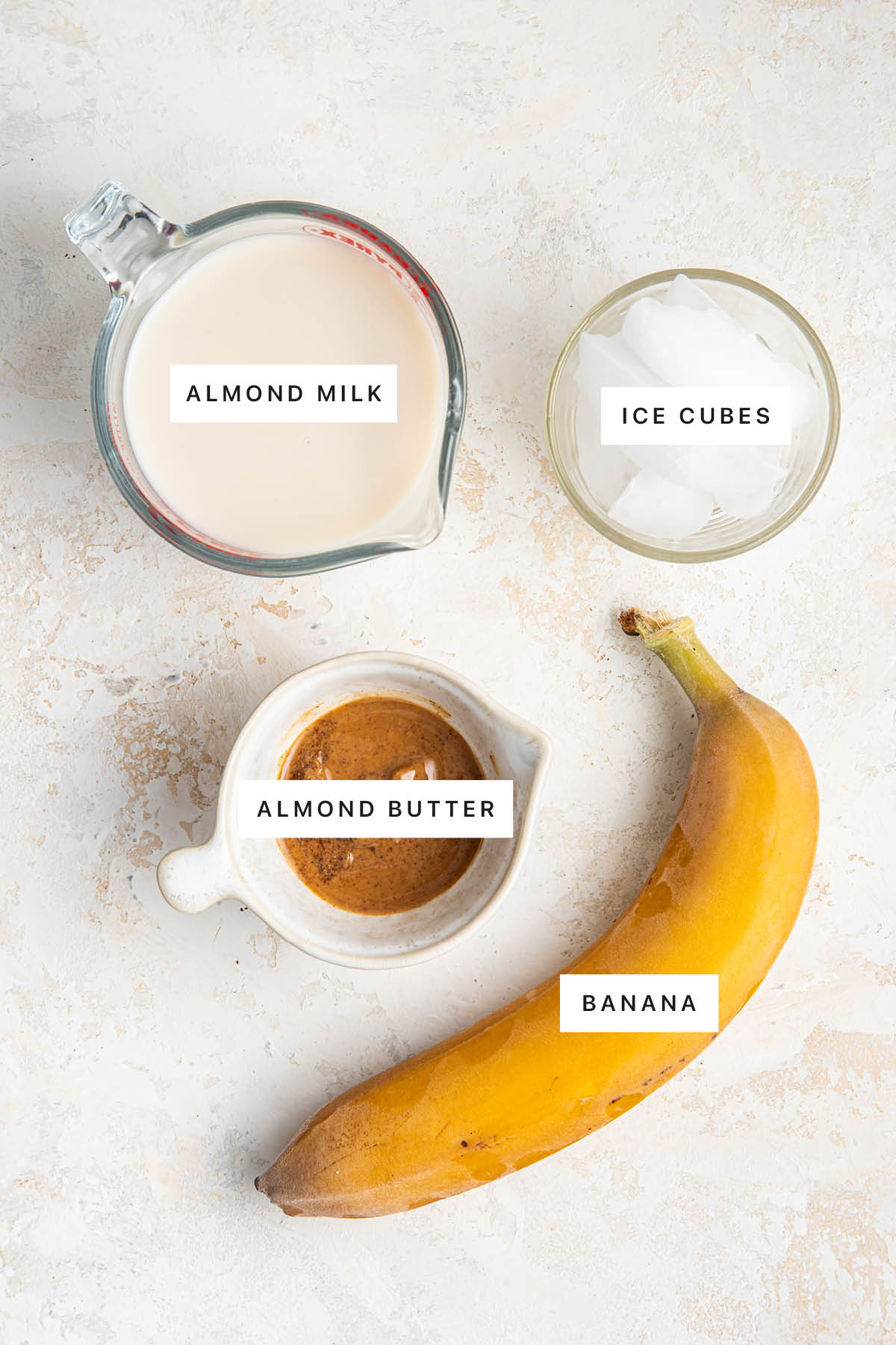 Ingredients measured out to make a Banana Almond Butter Smoothie: almond milk, ice cubes, almond butter and banana.