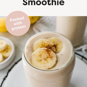 A banana smoothie in a glass, topped with fresh banana slices and a dash of cinnamon.