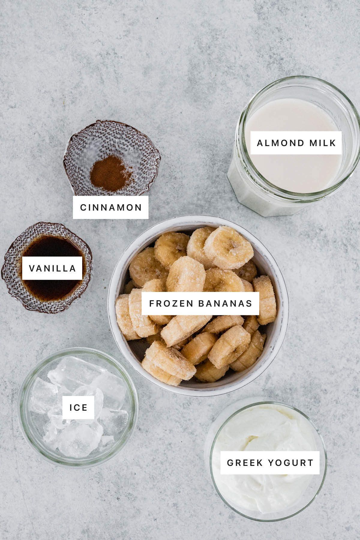 Ingredients measured out to make a Banana Smoothie: cinnamon, almond milk vanilla, frozen bananas, ice and Greek yogurt.