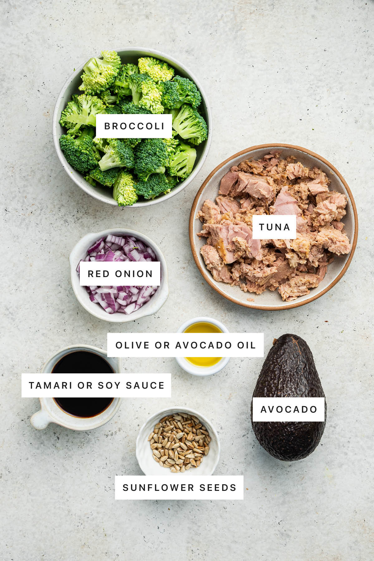 Ingredients measured out to make a Broccoli Avocado Tuna Bowl: broccoli, tuna, red onion, olive oil, tamari, sunflower seeds and avocado.