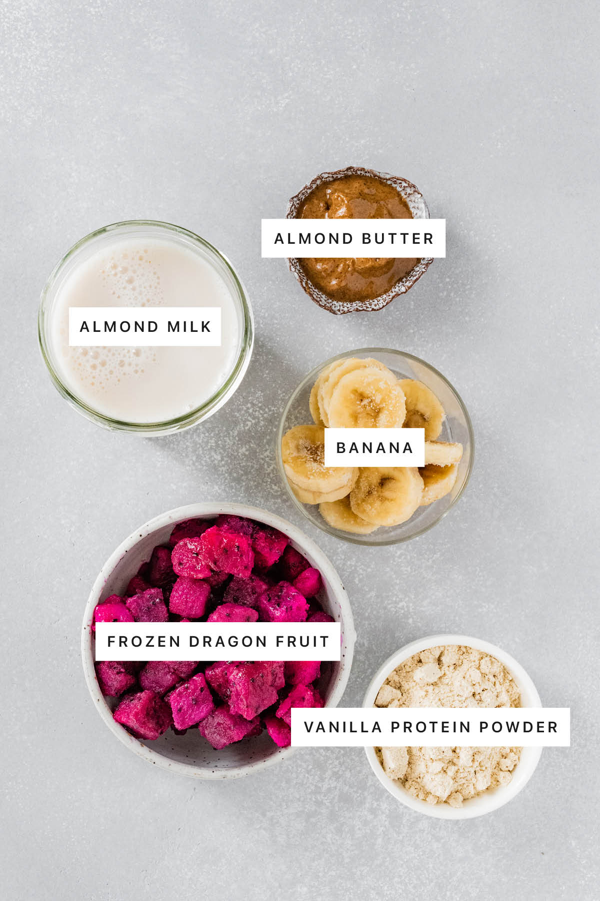 Ingredients measured out to make a Dragon Fruit Smoothie: almond butter, almond milk, banana, frozen dragon fruit and vanilla protein powder.