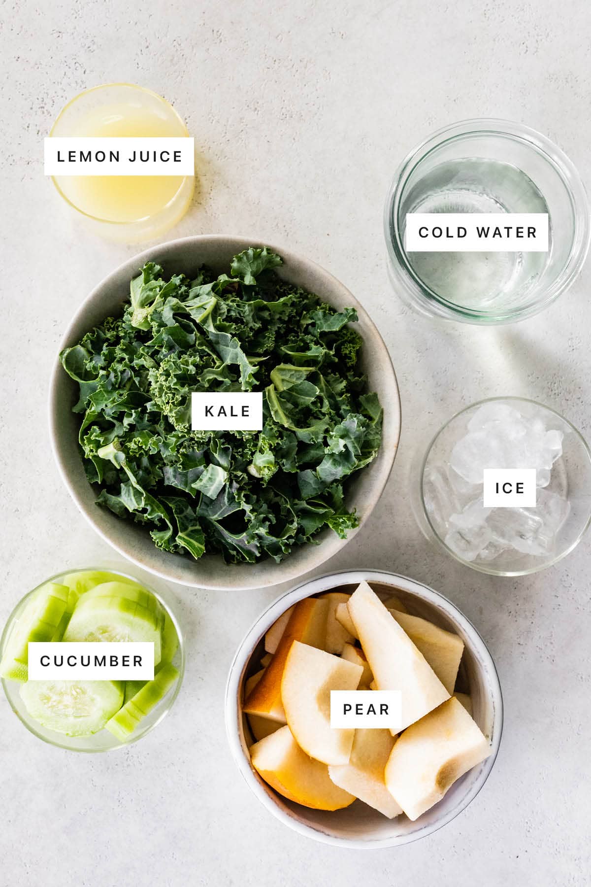 Measured ingredients to make a green lemonade smoothie: lemon juice, cold water, kale, ice, cucumber and pear.