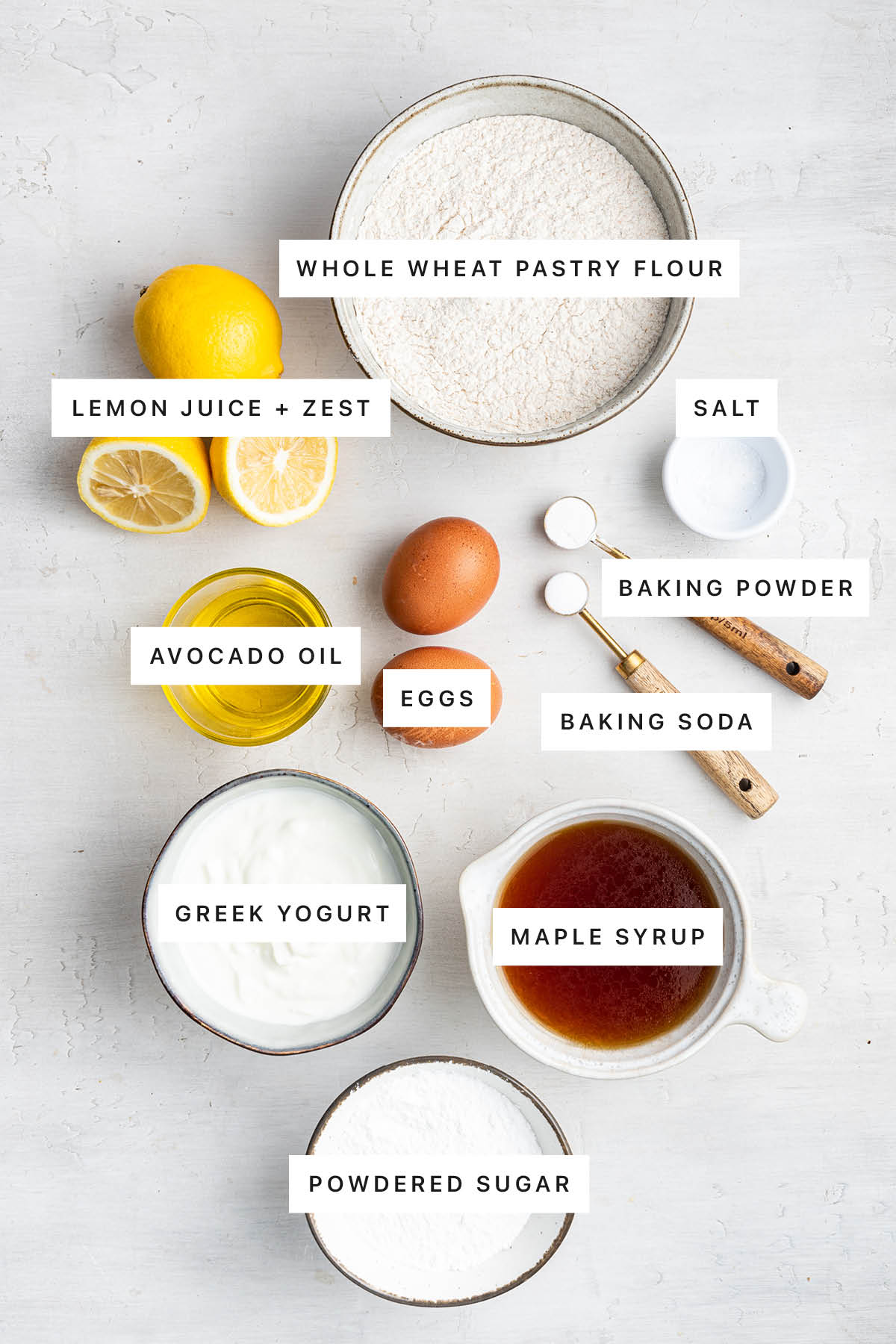 Ingredients measured out to make a lemon loaf: whole wheat pastry flour, lemon juice and zest, salt, avocado oil, eggs, baking powder, baking soda, Greek yogurt, maple syrup and powdered sugar.