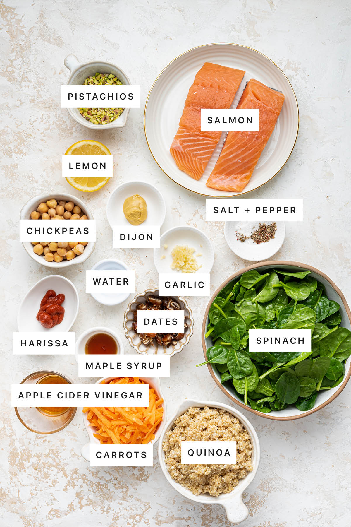 Ingredients measured out to make Pistachio Salmon Salad with Spicy Harissa Dressing: pistachios, salmon, lemon, dijon, chickpeas, salt, pepper, water, garlic, harissa, dates, spinach, maple syrup, apple cider vinegar, carrots and quinoa.