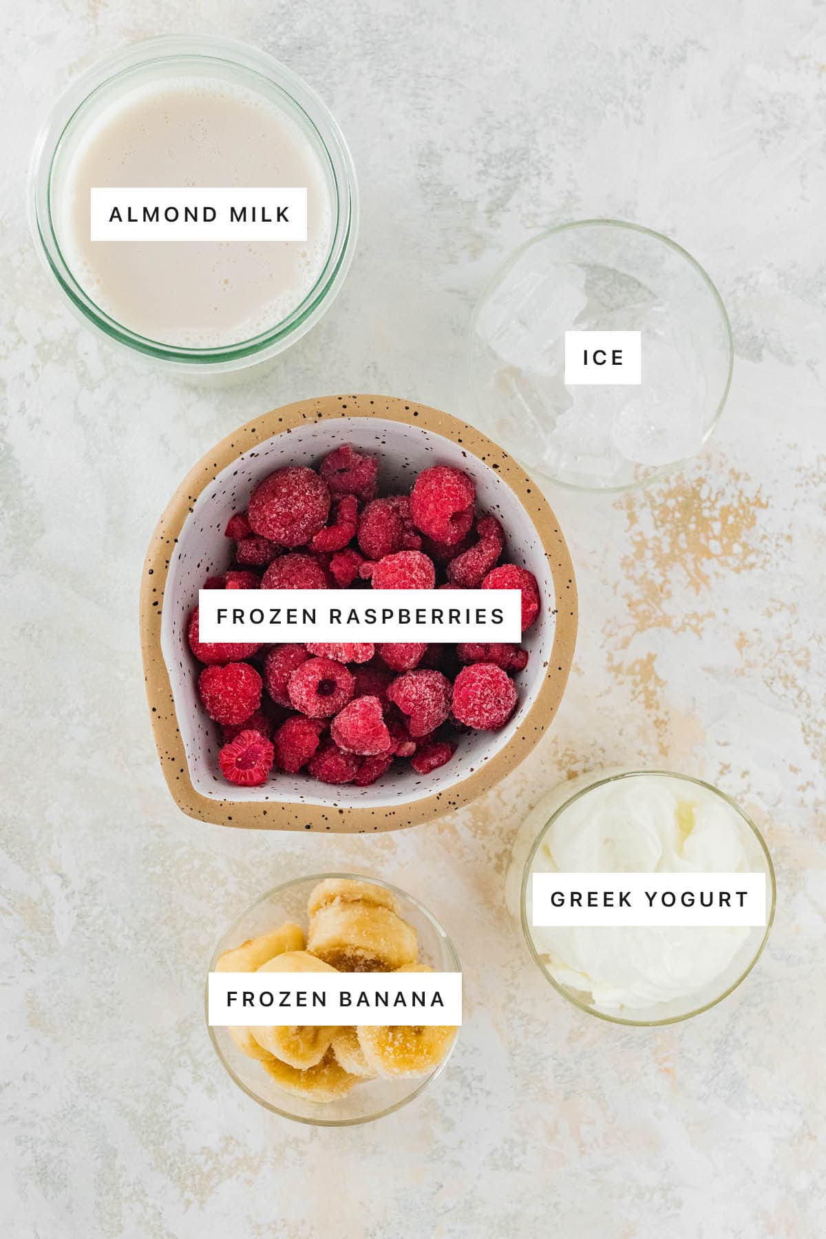 Ingredients measured out to make Raspberry Smoothie: almond milk, ice, frozen raspberries, frozen banana and Greek yogurt.