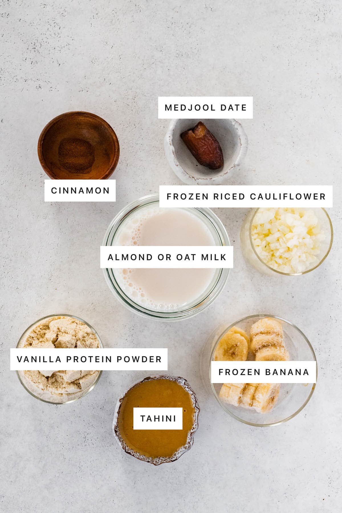 Ingredients measured out to make a Tahini Smoothie: cinnamon, medjool date, frozen riced cauliflower, almond or oat milk, vanilla protein powder, tahini and frozen banana.