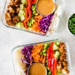 Two glass containers with the ingredients for the Asian noodle bowl including peanut baked tofu, red pepper, purple cabbage, edamame, rice noodles, celery, shredded carrots, and a sauce.