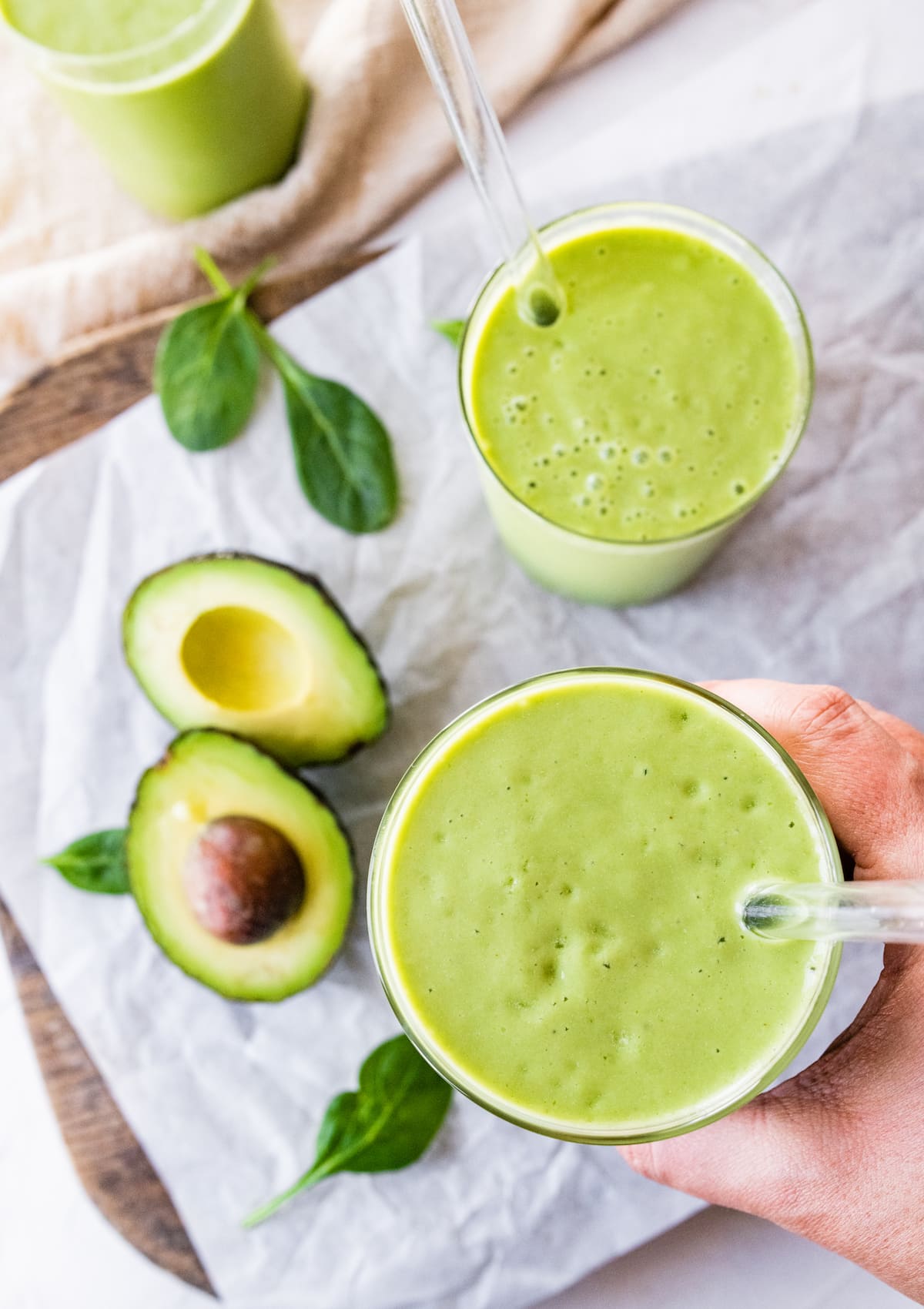 Woman's hand holding avocado smoothie with straw.