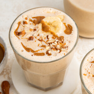 One glass filled with banana almond butter smoothie topped with banana slices, chopped almonds and a drizzle of almond butter.