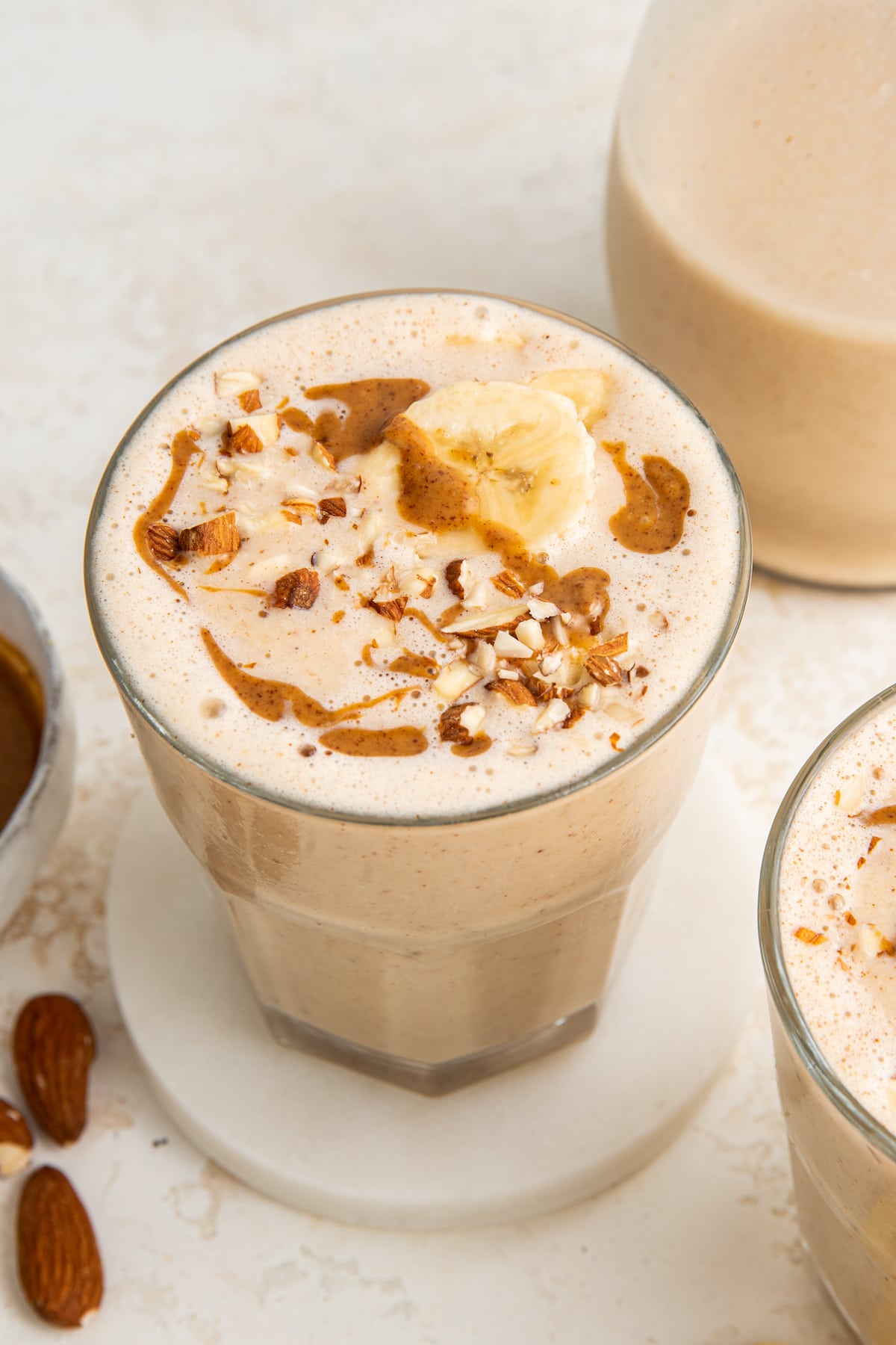 One glass filled with banana almond butter smoothie topped with banana slices, chopped almonds and a drizzle of almond butter.