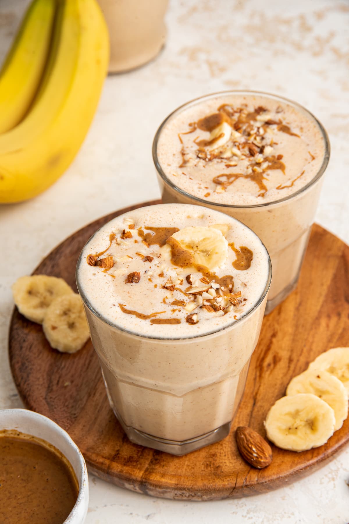 Two banana almond butter smoothies angled on a wooden board.