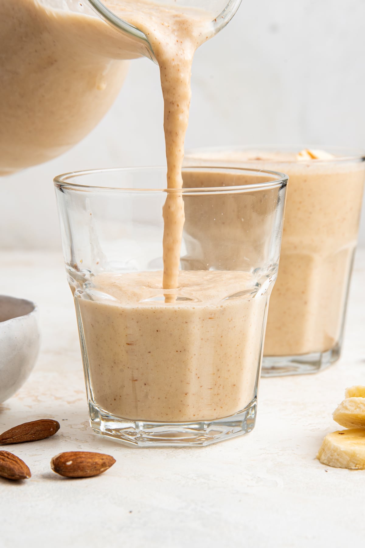 Banana almond butter smoothie being poured into glass cup.