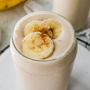 A banana smoothie in a glass, topped with fresh banana slices and a sprinkle of cinnamon.